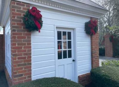 Clean white siding and red brick garden building with manicured hedges