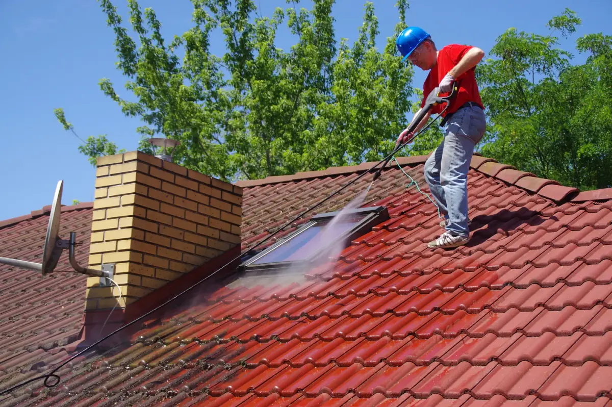 Technician soft washing a mossy tile roof to remove algae and buildup